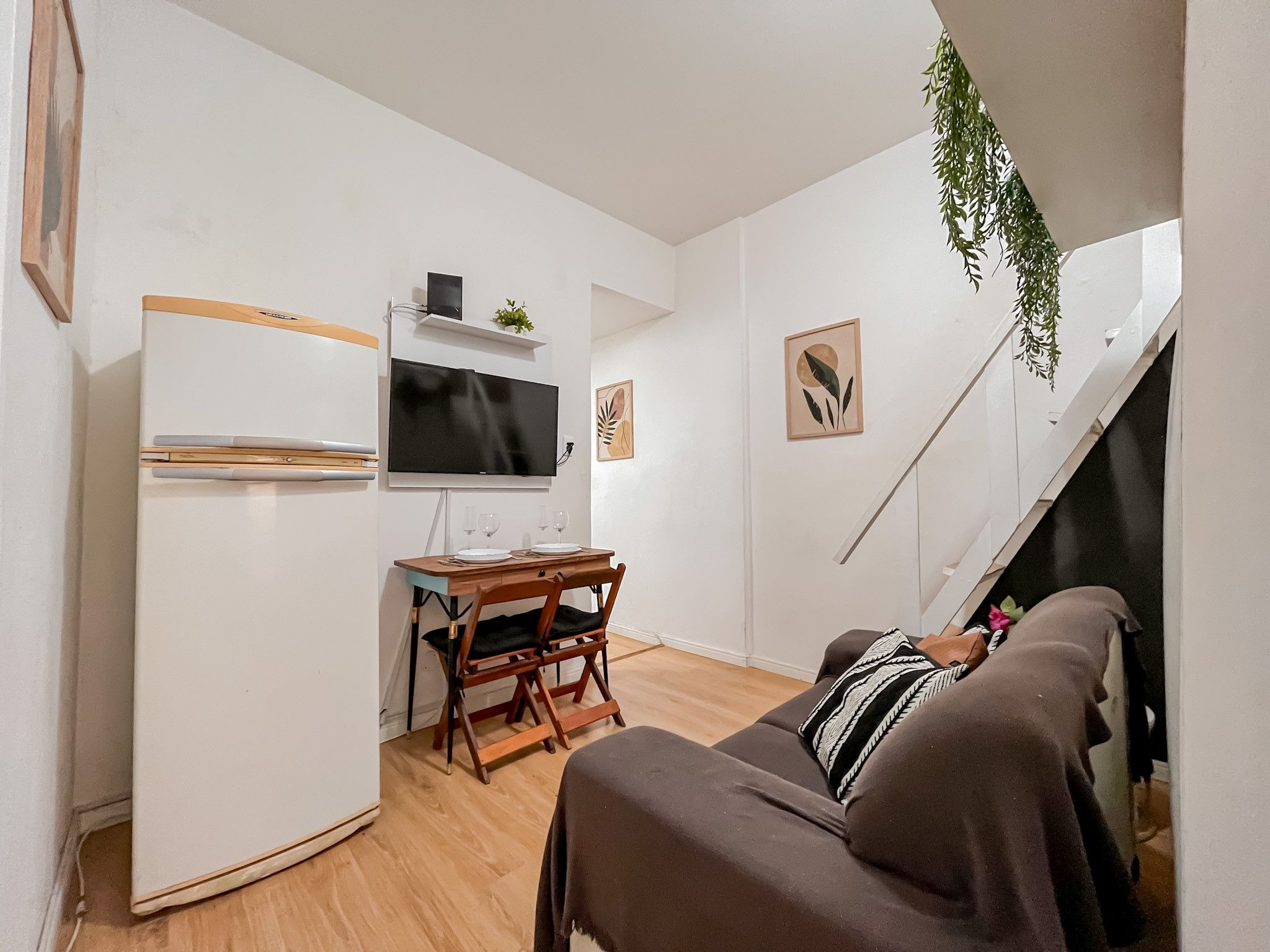 A compact living space with a kitchenette, a flat-screen TV, a dining table with chairs, a sofa, and a staircase.