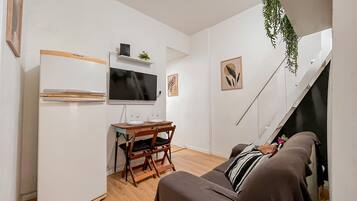 A compact living space with a kitchenette, a flat-screen TV, a dining table with chairs, a sofa, and a staircase.