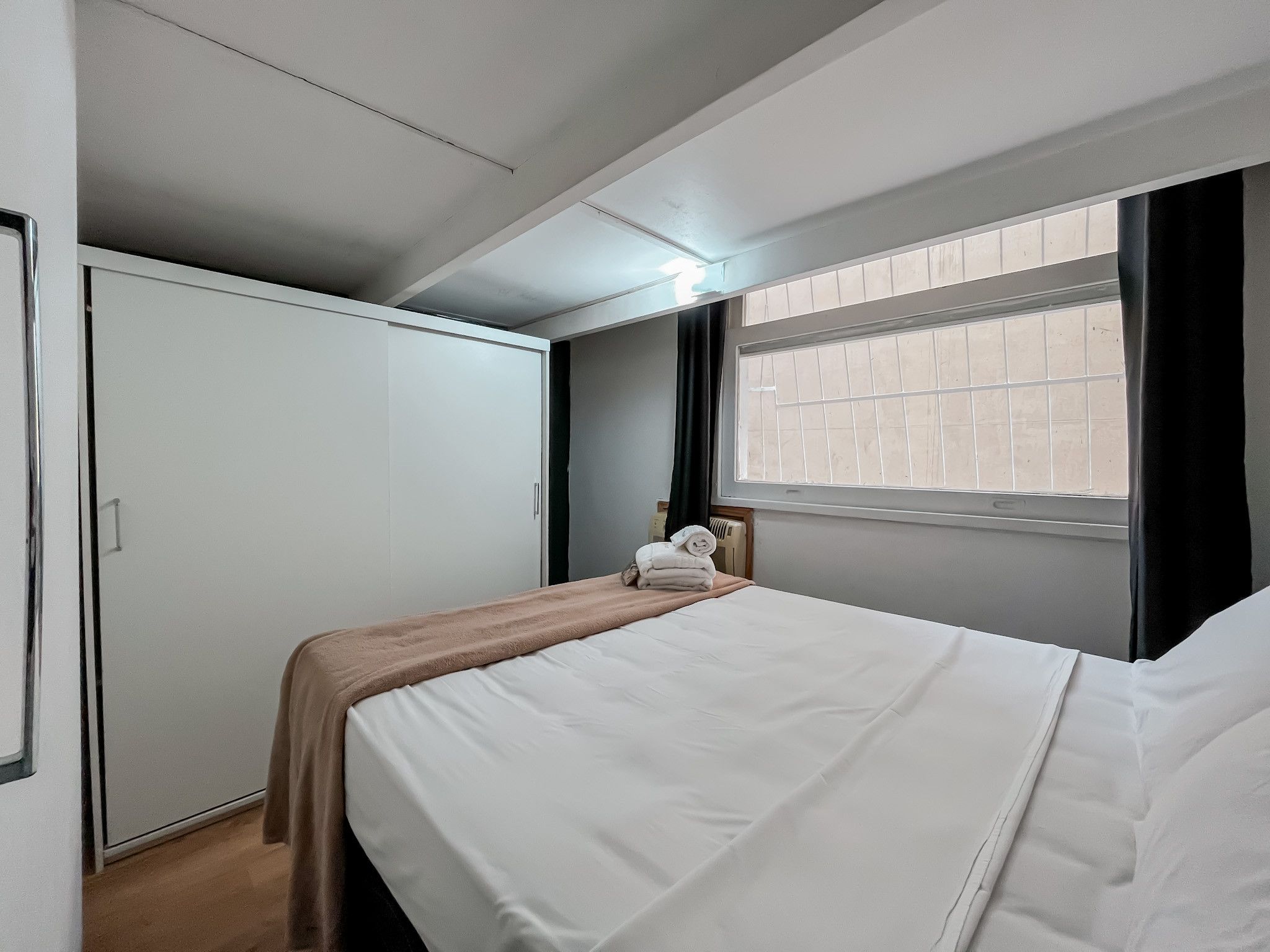 A hotel room with a bed, a wardrobe, a window with blinds, and a radiator.