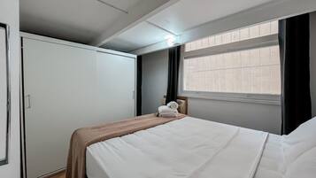 A hotel room with a bed, a wardrobe, a window with blinds, and a radiator.