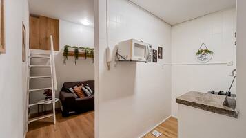 A compact living space with a kitchenette, a sofa, a ladder, and a small shelf.