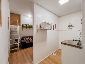 Un espacio habitable compacto con kitchenette, un sofá, una escalera y un estante pequeño.