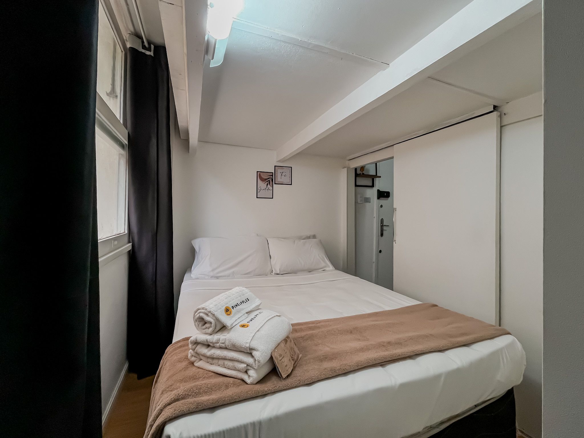 A hotel room with a bed, a window with curtains, a door, and a small wall decoration.