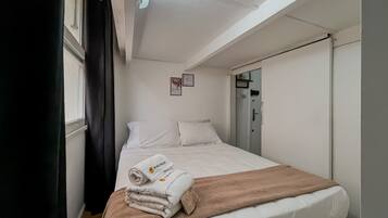 A hotel room with a bed, a window with curtains, a door, and a small wall decoration.