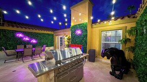 Un patio exterior con una parrilla de acero inoxidable, zona de estar y luces decorativas.