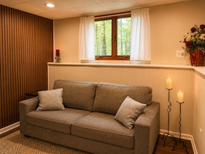 A neutral-toned sofa with patterned cushions, a window with white curtains, and a vase with flowers on a shelf. - Spacious 4BR Pocono Chalet - Hot Tub, Barrel Sauna & Game Room (Pocono Summit)