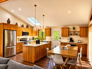 A modern kitchen with wooden cabinets, stainless steel appliances, a central island with seating, and pendant lighting. - Spacious 4BR Pocono Chalet - Hot Tub, Barrel Sauna & Game Room (Pocono Summit)