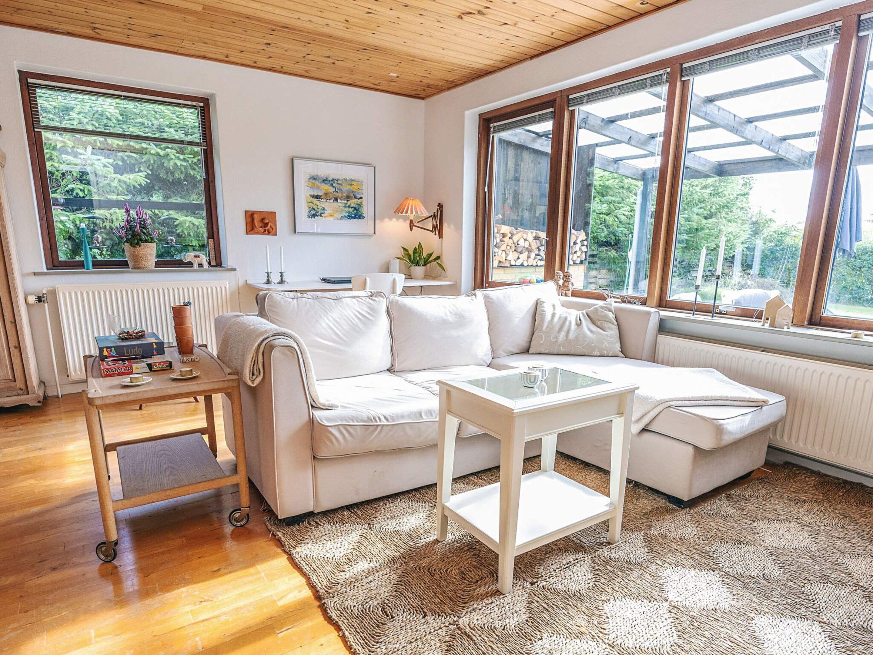 A cozy living room with a white sofa, a small table, and a large window offering a view of greenery.