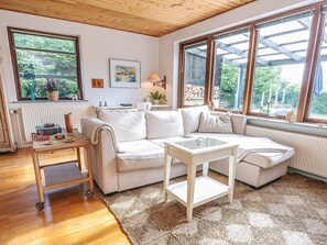 A cozy living room with a white sofa, a small table, and a large window offering a view of greenery. - 4 Person Holiday Home in Bindslev (Bindslev)
