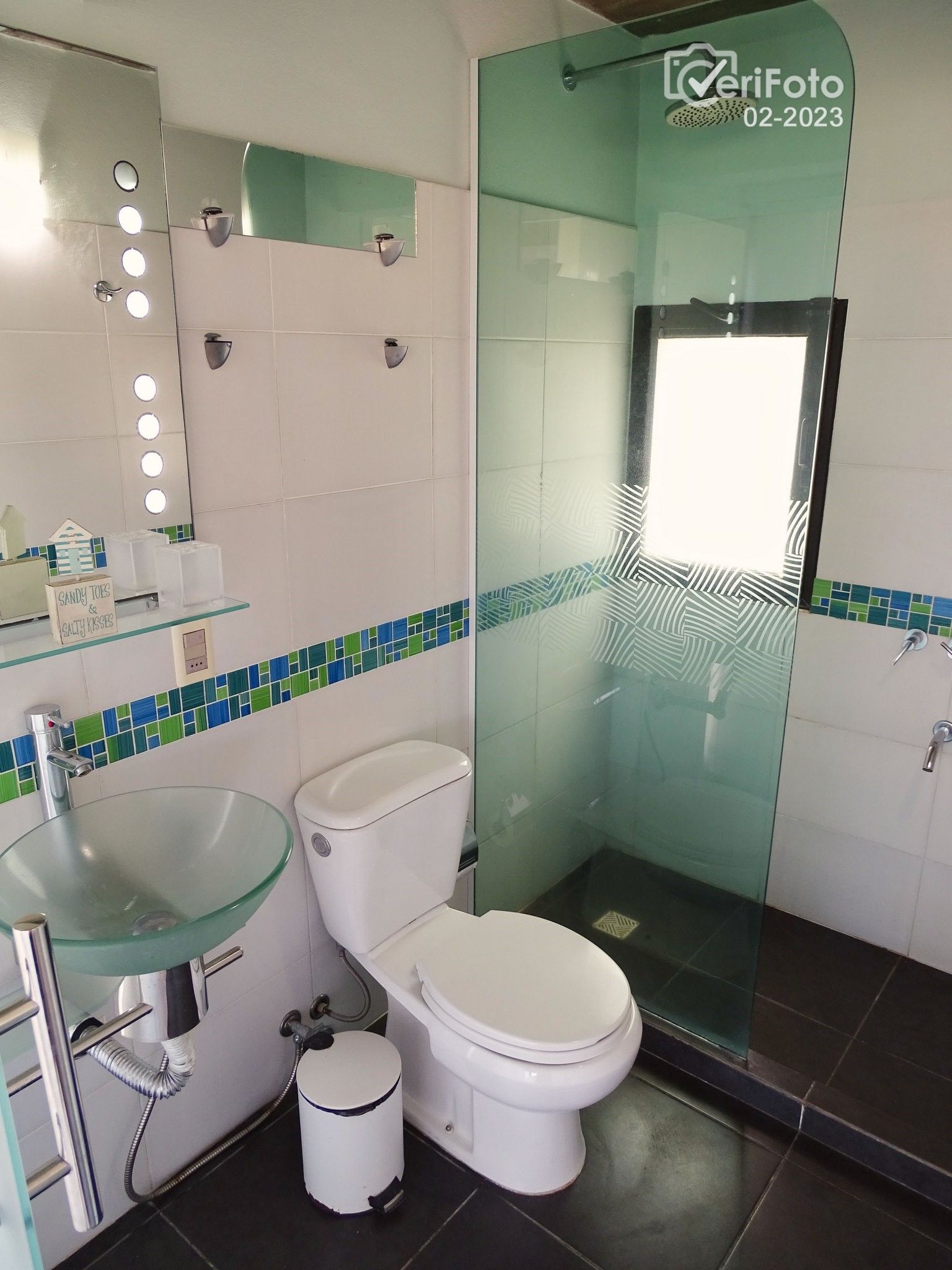 Et moderne badeværelse med vask af glas, hvidt toilet og brusekabine i glas.