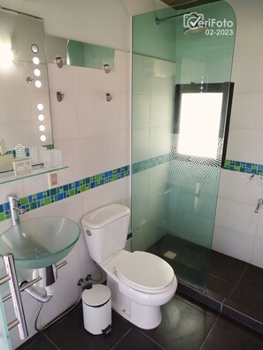 A modern bathroom with a glass sink, white toilet, and a glass shower enclosure.