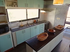 A kitchen with teal cabinets, a black countertop, a microwave, a stove, and a window with a view of trees.