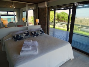 A bedroom with a large bed, two bedside lamps, a mirror, and a view of the outdoors.