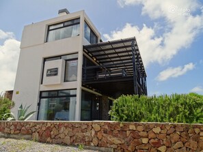 A modern two-story building with a stone facade, large windows, and a black metal structure on the second floor.