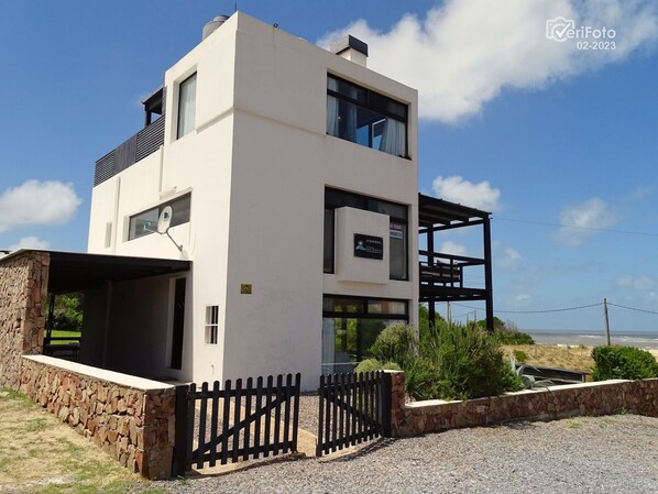 A modern two-story building with a stone foundation and a black metal fence.