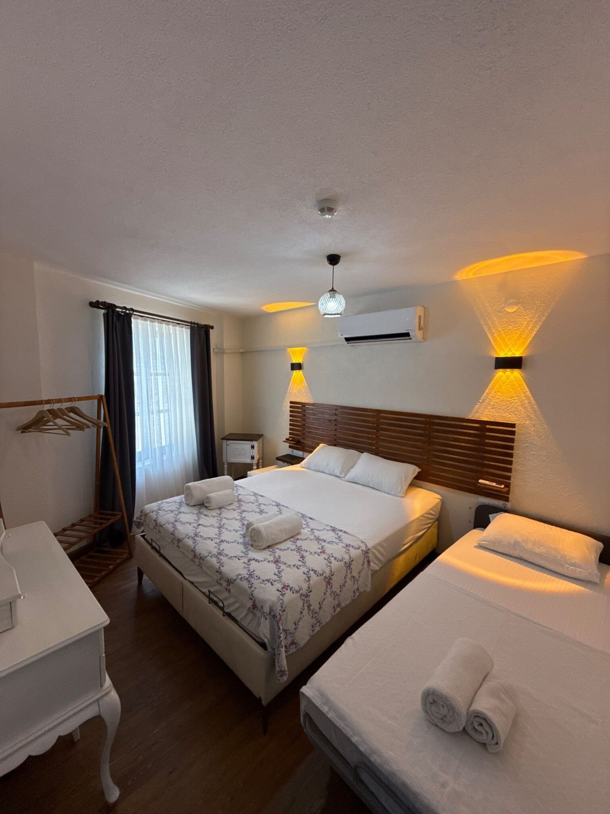 Una habitación de hotel con cama, escritorio, silla, armario y ventana con cortinas.