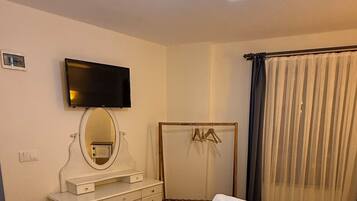 Una habitación de hotel con cama, cómoda, espejo, televisión y lámpara colgante.