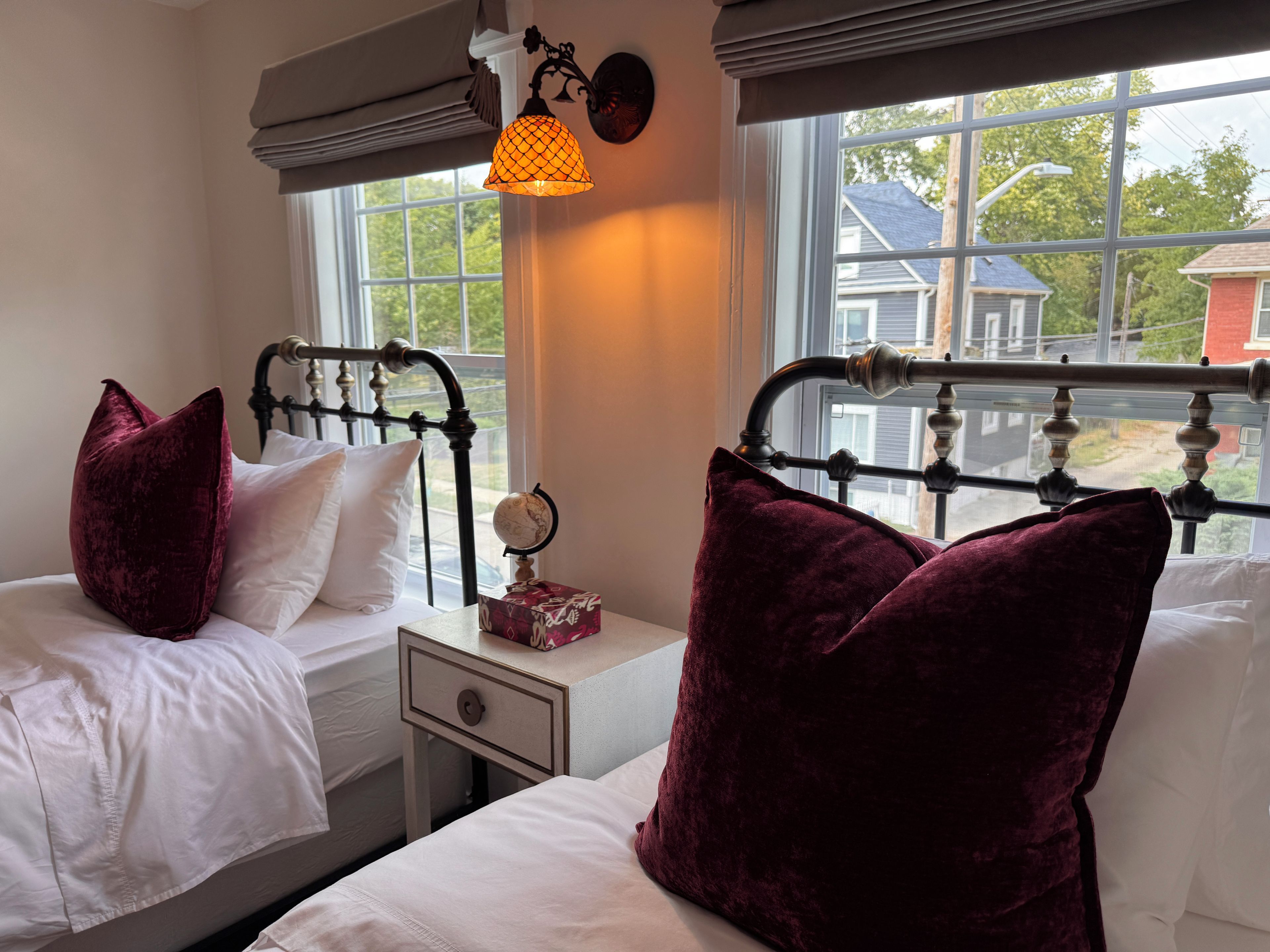 Een slaapkamer met twee bedden, een nachtkastje, een wereldbol en een raam met uitzicht op huizen.