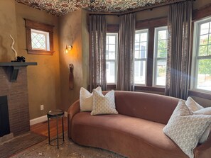 Una sala de estar acogedora con un sofá de cuero marrón, cojines estampados, una chimenea y un techo decorativo.