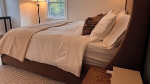 Un dormitorio con una cama grande, una mesita de noche, una lámpara y un ventanal con vistas a árboles.