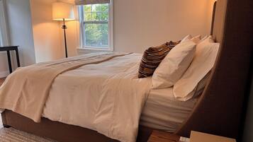A bedroom with a large bed, a bedside table, a lamp, and a window with a view of trees.
