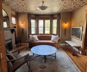 A room with a fireplace, a sofa, a round table, and a bench.