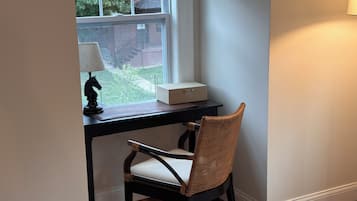A room with a desk, a chair, a lamp, and a window with a view of greenery.