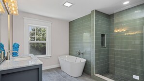 Un baño moderno con una bañera independiente, un ventanal grande y paredes con azulejos verdes.