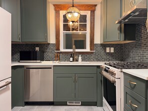 Una cocina con microondas integrado, electrodomésticos de acero inoxidable, ventana con marco de madera y salpicadero de azulejos hexagonales.