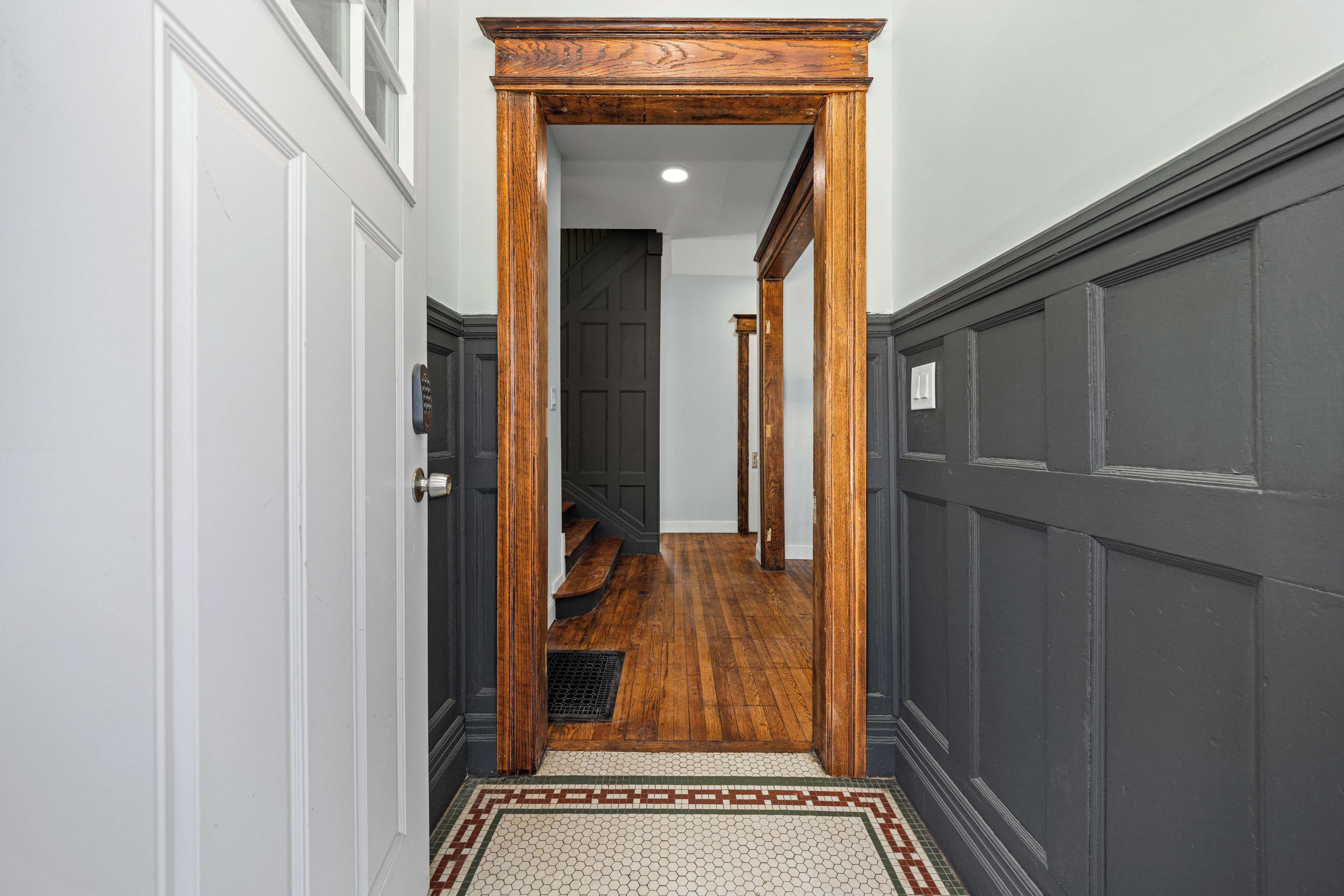 Un couloir étroit avec des portes en bois, un sol carrelé et un tapis à motifs.