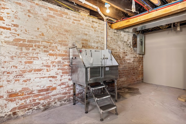 A utility room with exposed brick walls, a metal water heater, and a concrete floor.