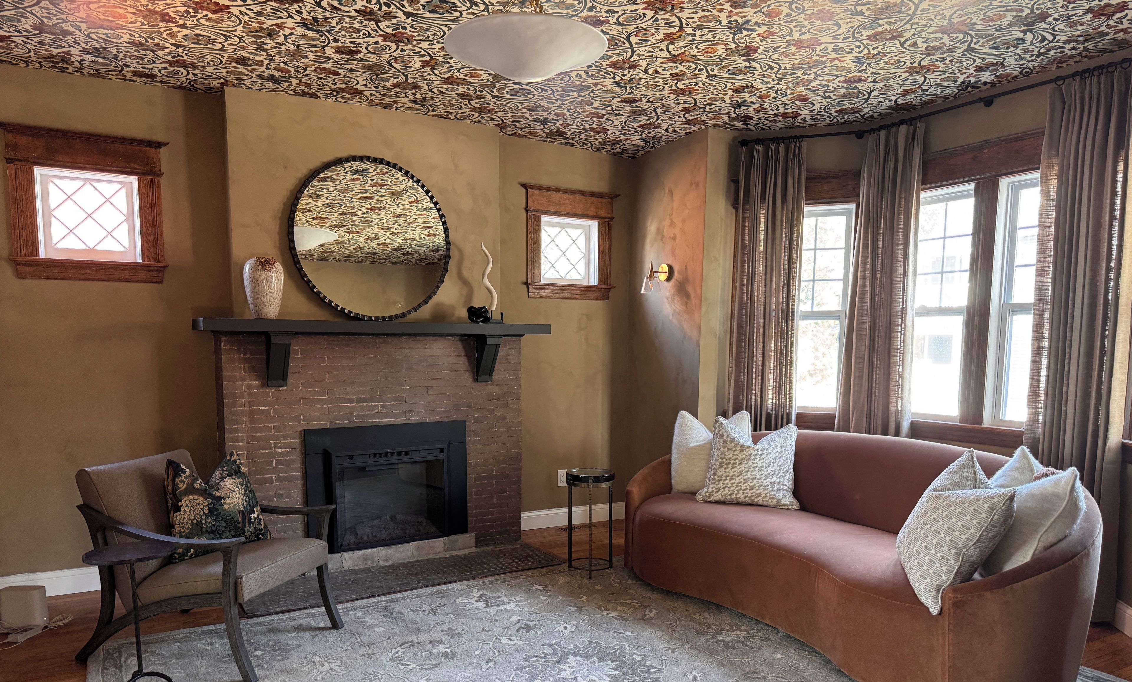 Een woonkamer met een open haard, een bank, een fauteuil en een decoratief plafond.