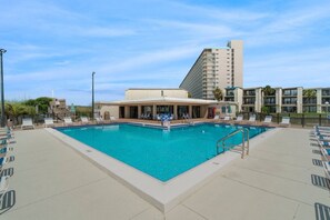 Piscina com espreguiçadeiras e um edifício ao fundo.