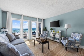 A living room with a sofa, armchair, coffee table, and a TV on the wall. - Emerald Escape at Sugar Beach C27 - Gulf Views, Beachfront Pool, Private Balcony (Panama City Beach)