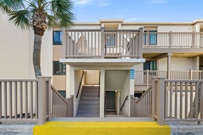 A multi-story building with a central staircase, balconies, and a palm tree. - Emerald Escape at Sugar Beach C27 - Gulf Views, Beachfront Pool, Private Balcony (Panama City Beach)
