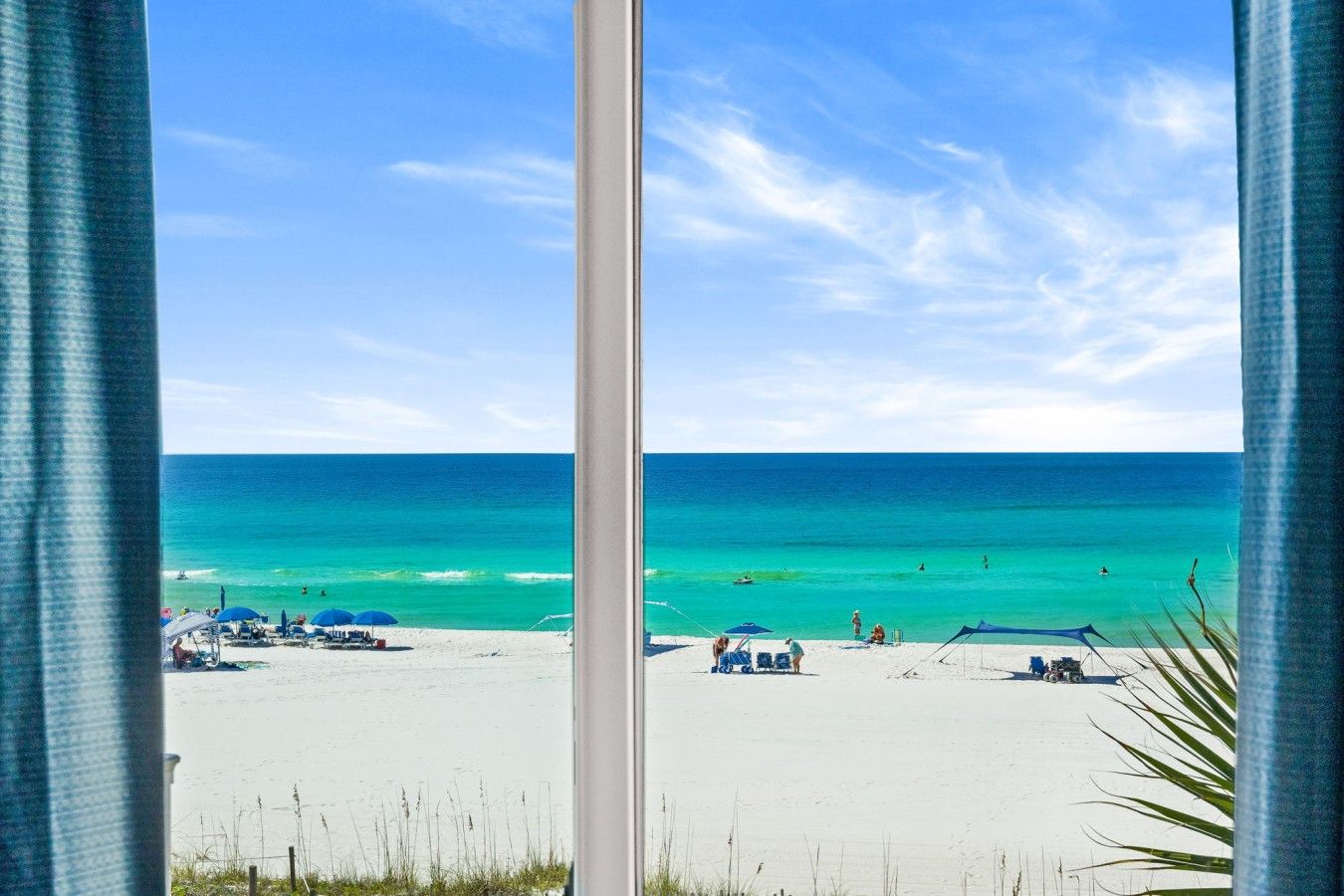 Vista a la playa a través de una ventana, con cielo despejado y mar tranquilo.
