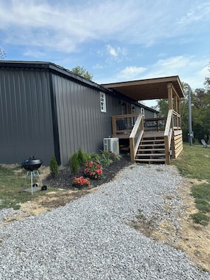 A building with a covered porch, a gravel driveway, and a barbecue grill.
