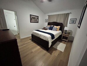 Ein Schlafzimmer mit Bett, Nachttisch, Lampe und einer Tür.