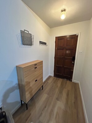 Un couloir avec une commode en bois, une porte et un luminaire au plafond.