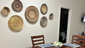 A dining area with a wooden table, six chairs, and decorative woven plates on the wall. - Furnished 2BR + Office/Guest Room Near Texas Health HEB & DFW Airport (Bedford)