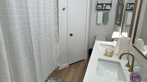 A bathroom with a shower, a sink with a mirror, and a toilet. - Furnished 2BR + Office/Guest Room Near Texas Health HEB & DFW Airport (Bedford)