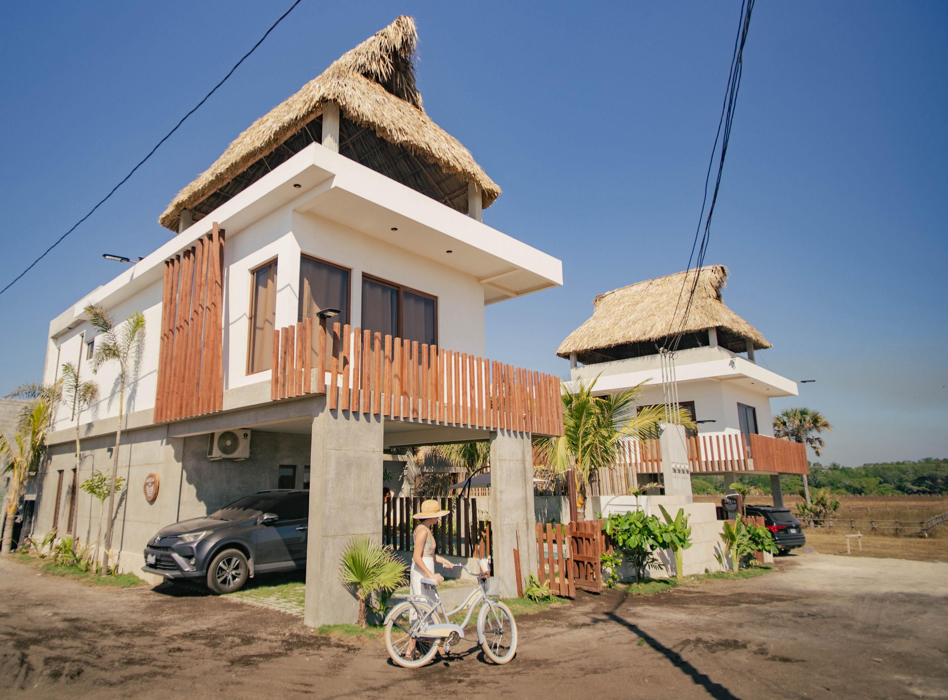 Una casa moderna de dos pisos con techo de paja, un balcón y una bicicleta estacionada adelante.