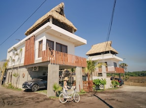 A modern two-story house with a thatched roof, a balcony, and a bicycle parked in front.