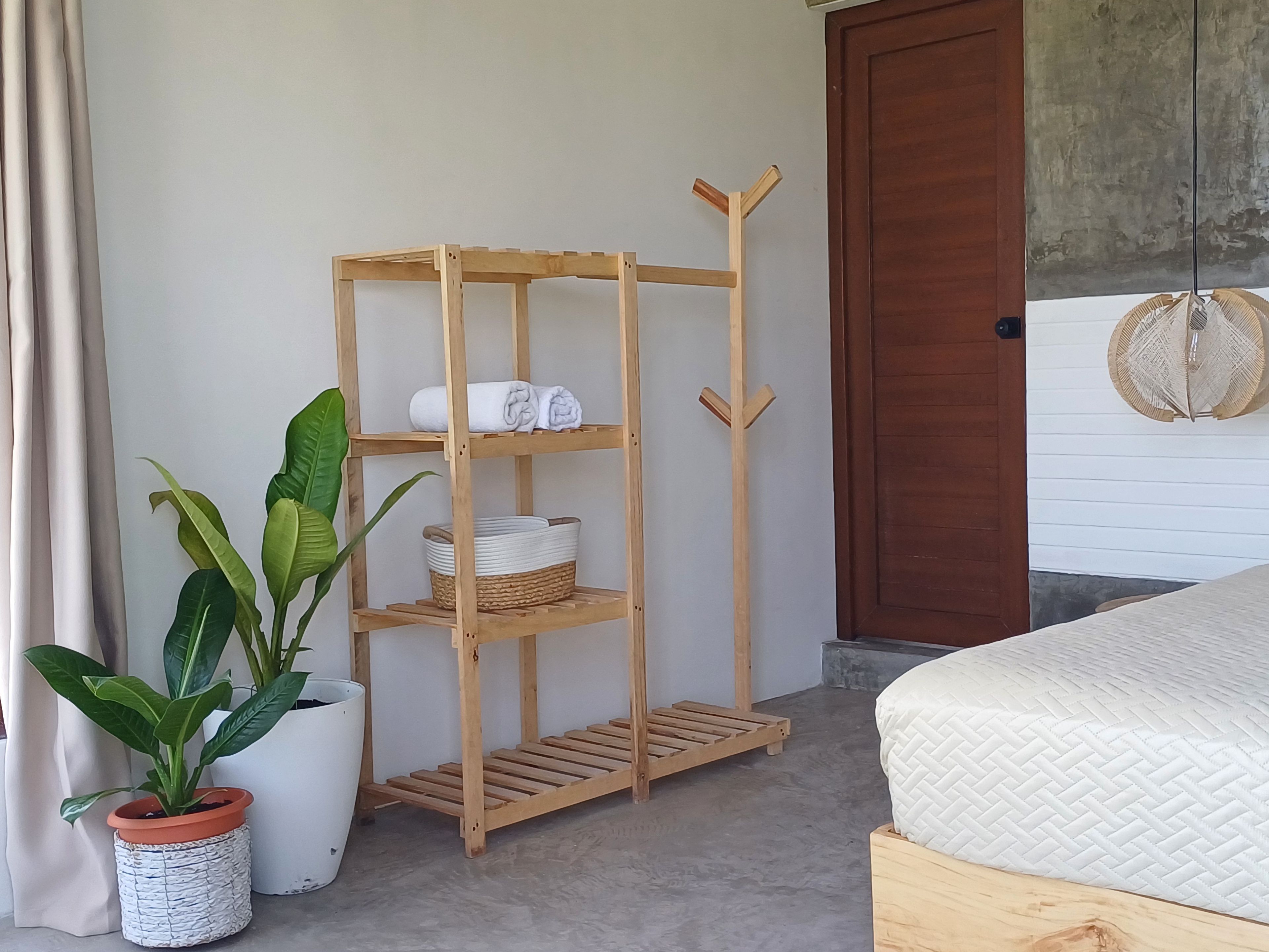 A wooden shelf unit with towels and baskets, a potted plant, and a bed with a textured mattress.
