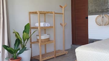 A wooden shelf unit with towels and baskets, a potted plant, and a bed with a textured mattress.