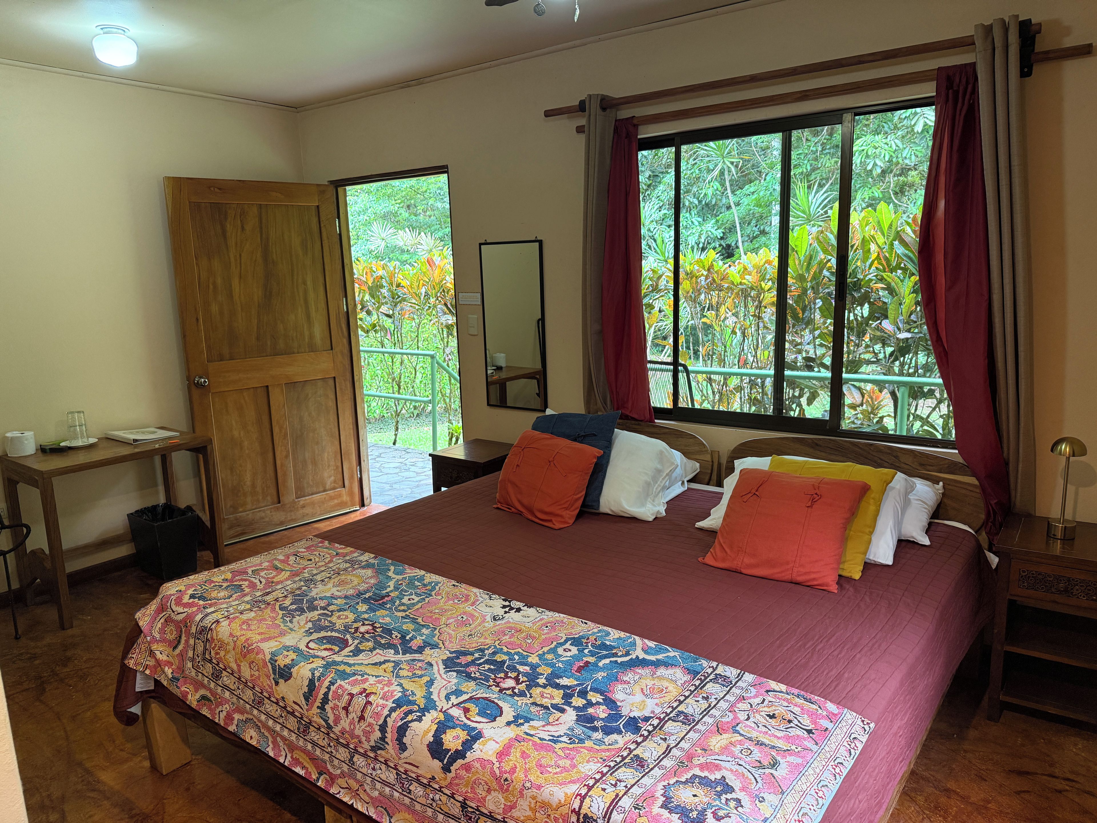 A bedroom with a large bed, a wooden door, a small table, and a window with curtains.