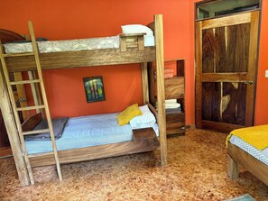 Una cama litera con escalera, una mesita de noche pequeña, un estante con toallas dobladas y una puerta con panel de madera.