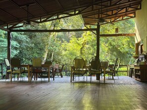 Eine überdachte Terrasse im Freien mit Holzboden, Metallstühlen und einem Tisch.