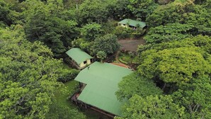 A secluded property surrounded by dense forest, featuring a main building with a green roof and a smaller structure nearby. - Rainforest Riverside Retreat Lake Arenal. Enjoy your family & friends getaway! (Tilaran)