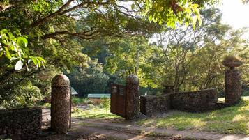 Une porte en pierre au design traditionnel, qui mène à un sentier bordé d’une végétation luxuriante et d’arbres.